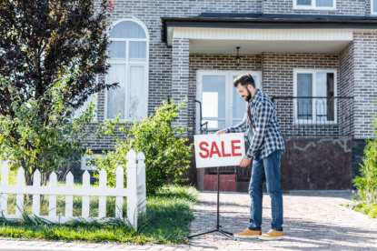 A man adding a for sale sign outside of his home