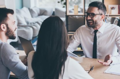 A mortgage advisor smiling and talking with a couple at a desk