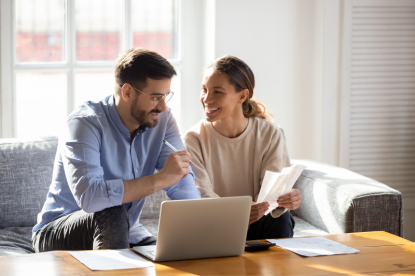 A couple smiling over paperwork and a laptop in their living room